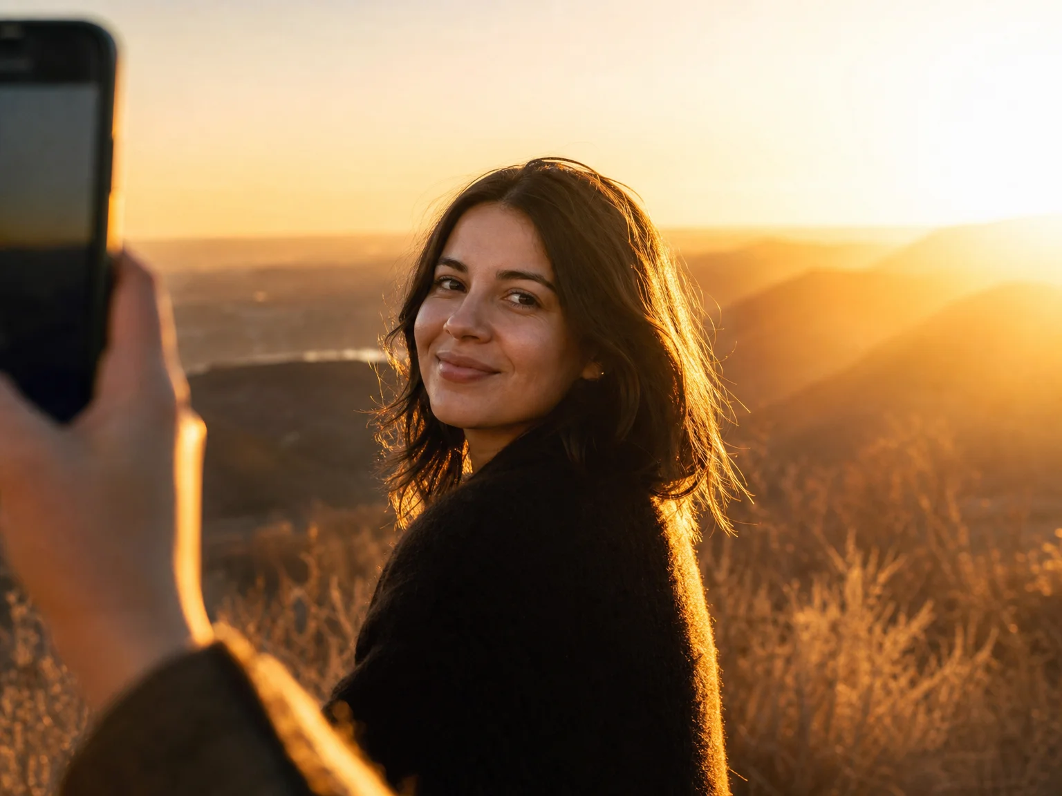 A candid portrait at golden hour showing a rim-light setup: the subject stands angled to a low sun behind and to one side, with a bright edge of light along their hair and shoulder while their face stays clearly lit