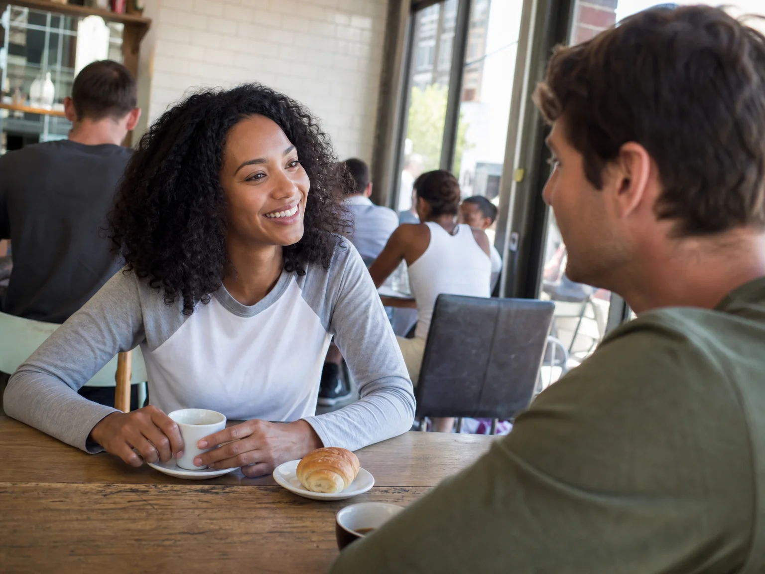 Two adults meeting for the first time at a daytime coffee shop, sitting near a window and talking