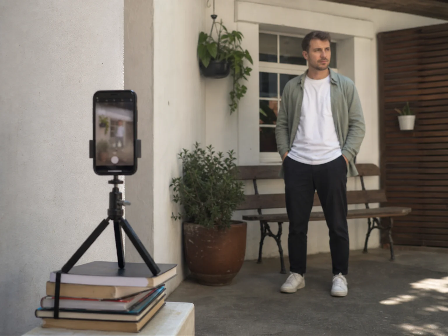 A smartphone propped on a small tripod with a self-timer counting down while a man waits a few steps away in natural daylight