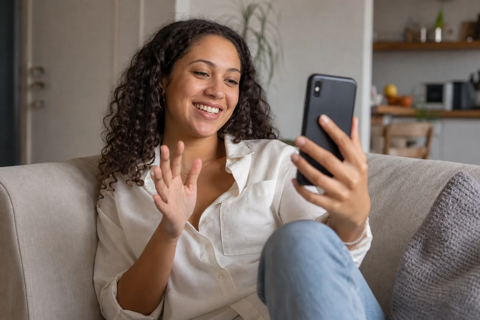 A woman smiling on a video call with her smartphone in a sunlit living room
